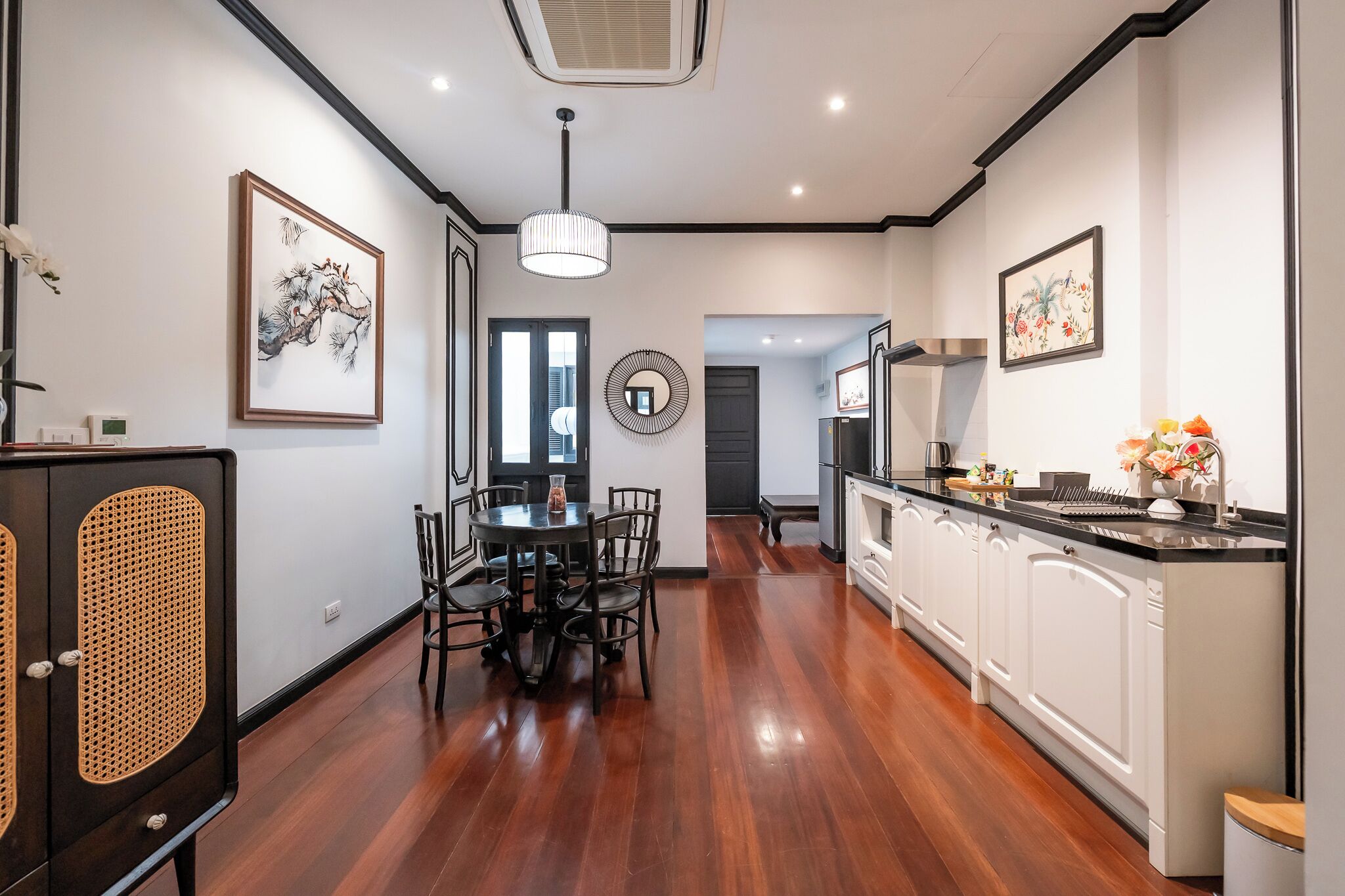 A modern kitchen with a dining area, wooden flooring, white cabinetry, and artwork on the walls.