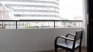 A balcony with a black chair, a white wall, and a view of a multi-story building.