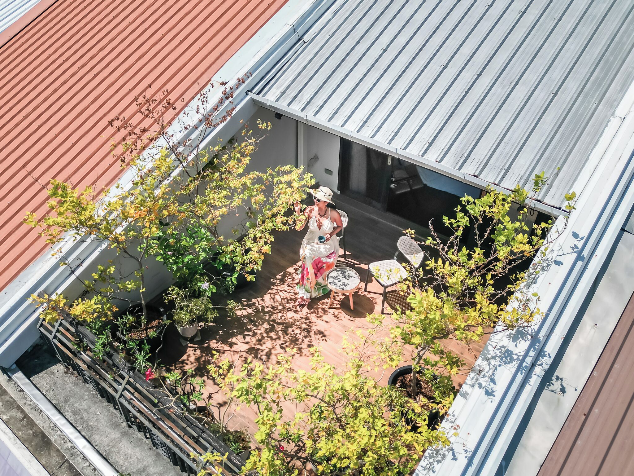 A rooftop patio with a seating area, potted plants, and a person sitting at a table.