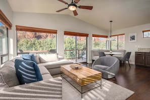 A spacious living area with a sofa, armchair, and coffee table, large windows with a view of red rock formations, and a ceiling fan.