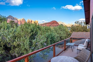 A balcony with a view of red rock formations, a table, and two chairs.