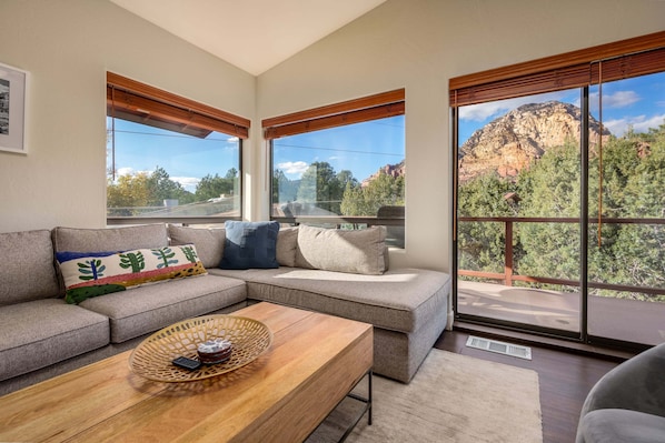 A modern living room with a sectional sofa, a wooden coffee table, and large windows offering a mountain view.