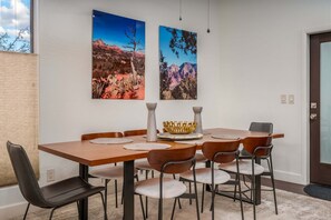 A dining area with a wooden table, six chairs, two wall-mounted paintings, and a decorative bowl. - Walk to Sedona Trails | Red Rock Views | Hot Tub | Private Casita (Sedona)