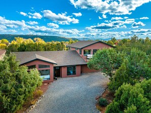 A two-story house with a gravel driveway and a view of the surrounding forest. - Walk to Sedona Trails | Red Rock Views | Hot Tub | Private Casita (Sedona)