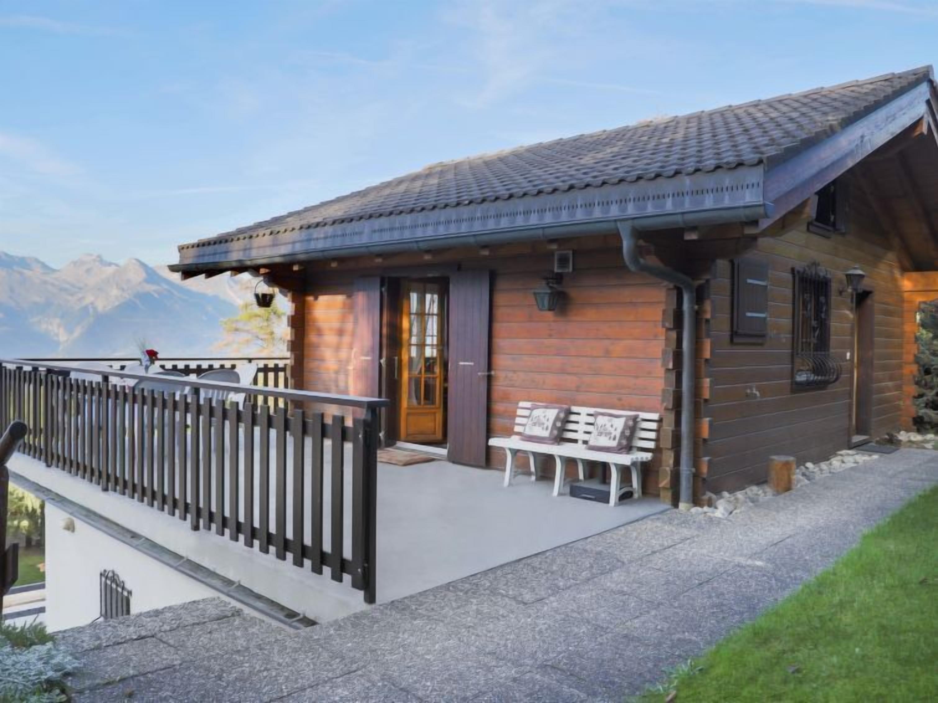 A wooden cabin with a balcony, a bench, and a mountain view.
