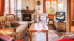 Un salon chaleureux avec une cheminée, un canapé, une table recouverte d’une nappe à carreaux et un téléviseur.