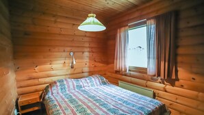 A wooden cabin room with a bed, a window with curtains, and a hanging light fixture. - Pihatupa 2 by Interhome (Kuusamo)