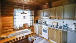 A cozy cabin-style kitchen with wooden walls, a dining table, and basic appliances. - Pihatupa 2 by Interhome (Kuusamo)