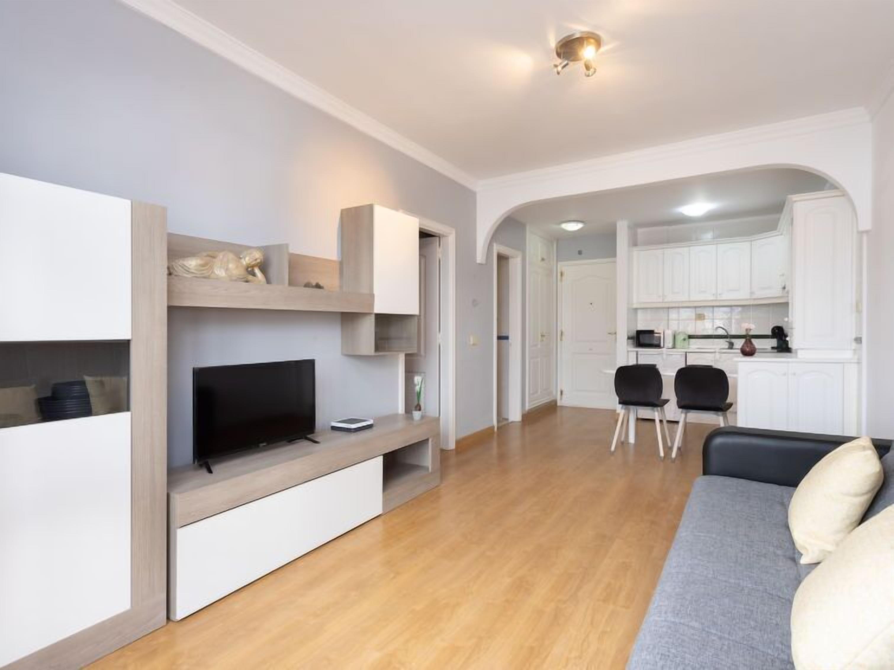 A modern living room with a flat-screen TV, built-in shelves, and a grey sofa.