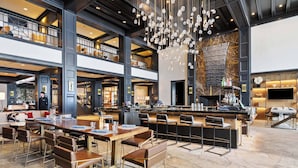 A spacious, modern hotel lobby with a high ceiling, a central bar area, and multiple seating options.