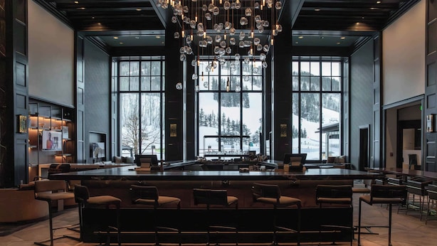 A spacious bar area with a long counter and multiple seating options, large windows offering a view of a snowy landscape, and a modern chandelier.