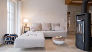 Un salon moderne avec un canapé, un pouf et un poêle à bois noir.
