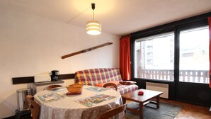 Una sala de estar acogedora con una mesa de comedor, sillas, un sofá y un amplio ventanal con cortinas.