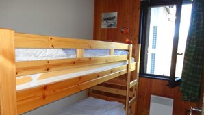Una cama litera en una habitación con paredes de madera, una ventana y un radiador.