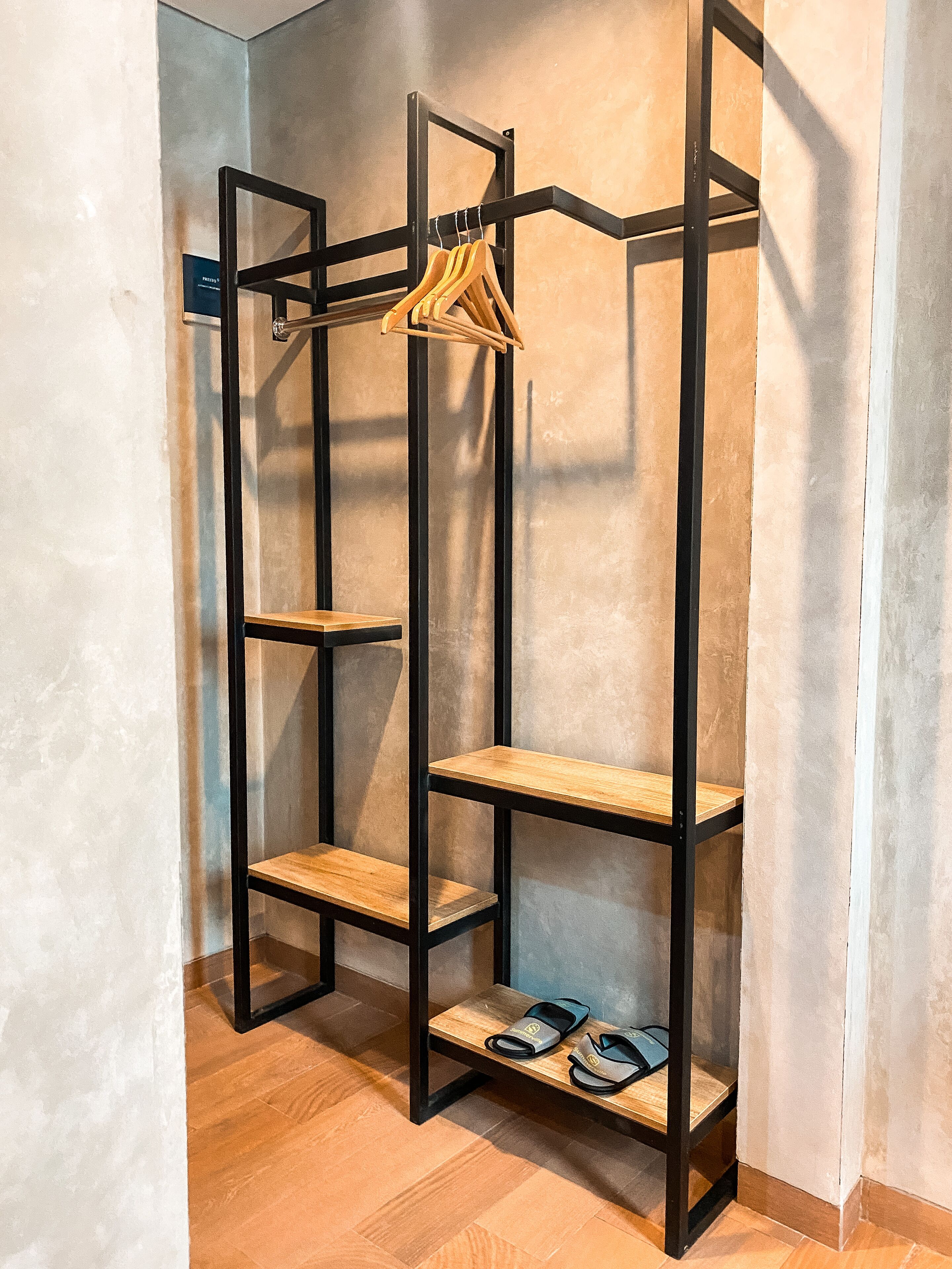 Een hoge, zwarte metalen rek met houten planken en een hangroede, in een ruimte met een houten vloer en eenvoudige muren.