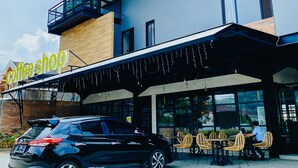 Un edificio moderno con una cafetería en la planta baja, que cuenta con un área de estar al aire libre cubierta y un coche negro estacionado en la parte delantera.