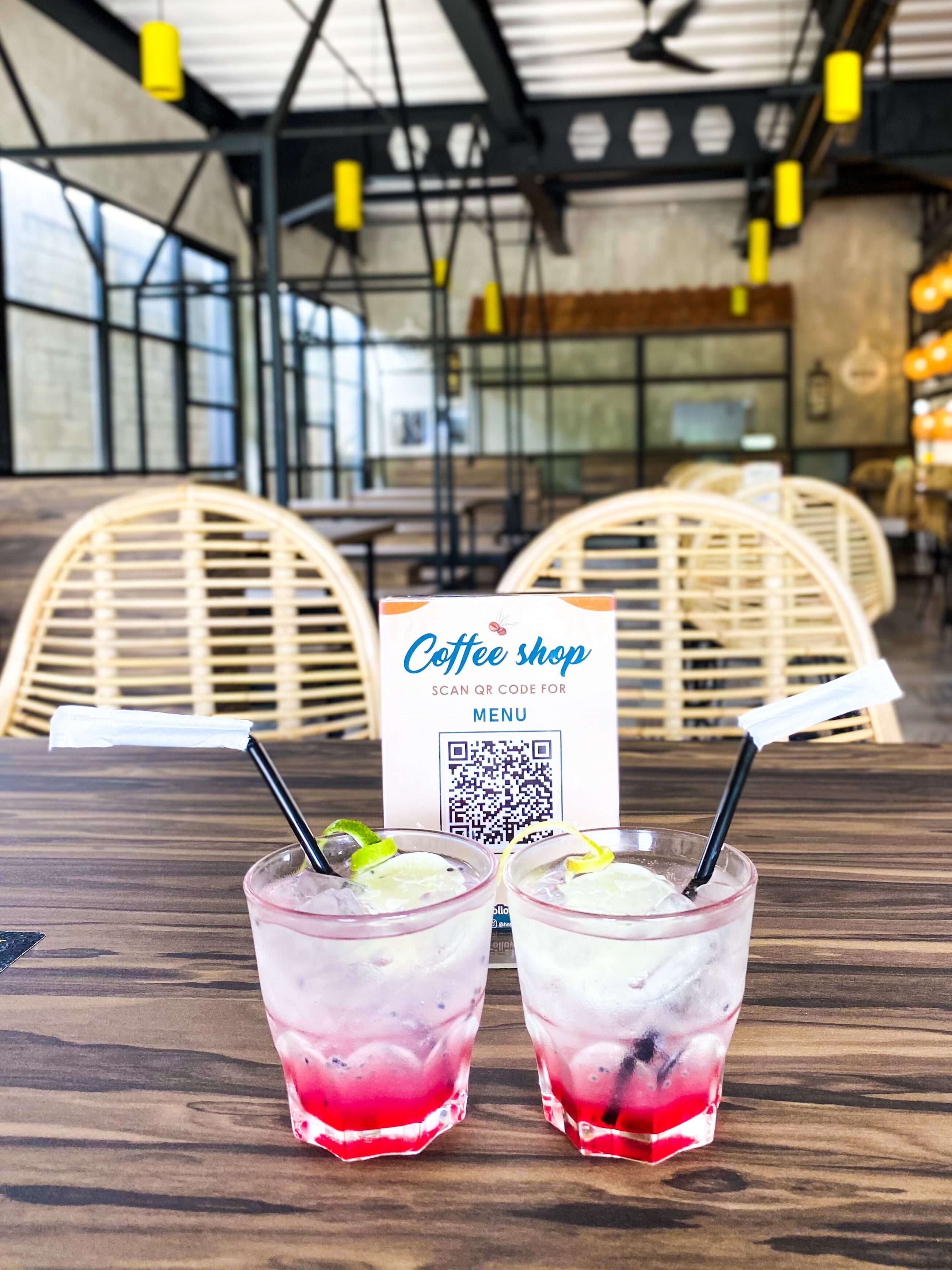 A coffee shop interior with two drinks on a table, a QR code menu sign, and wicker chairs.