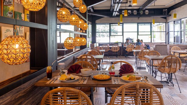 Un restaurante con sillas de mimbre, mesas de madera y lámparas colgantes de mimbre.