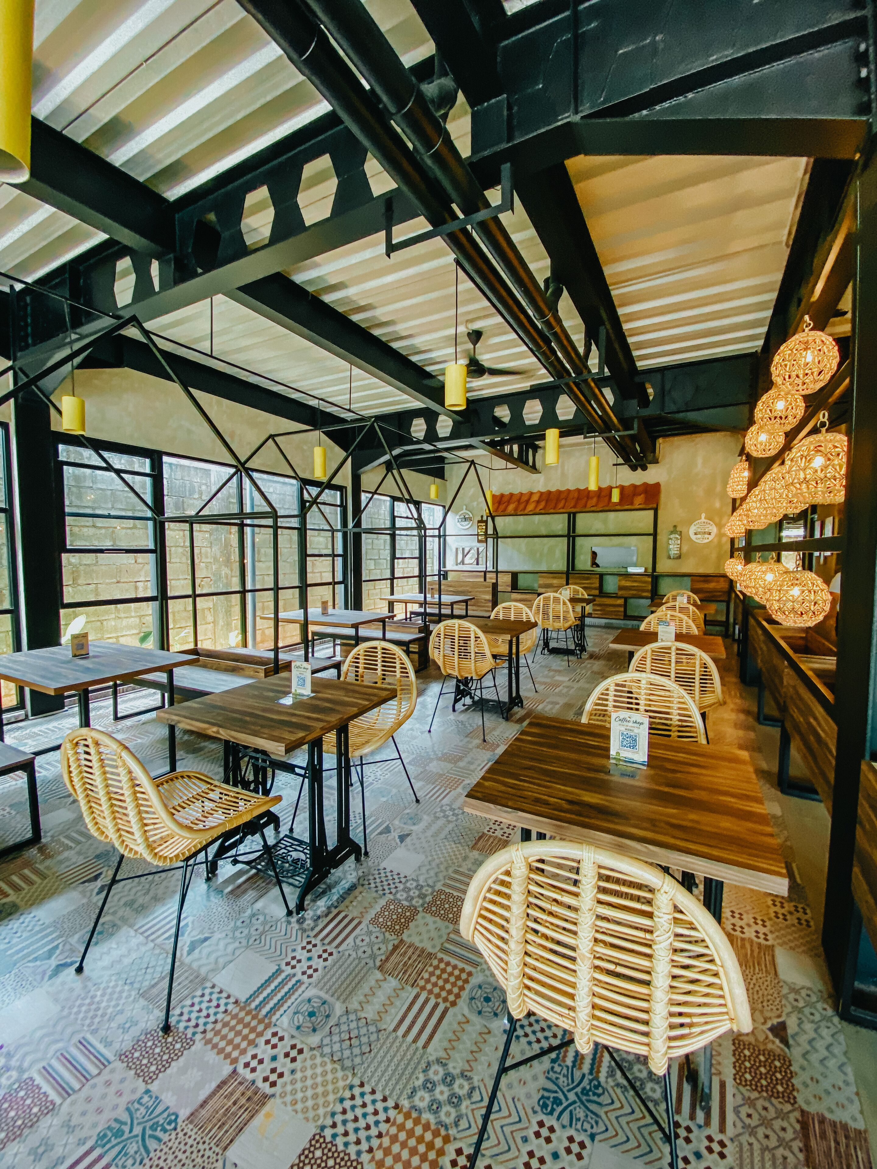 A spacious cafe with high ceilings, exposed beams, and large windows. Tables and chairs are arranged for seating.