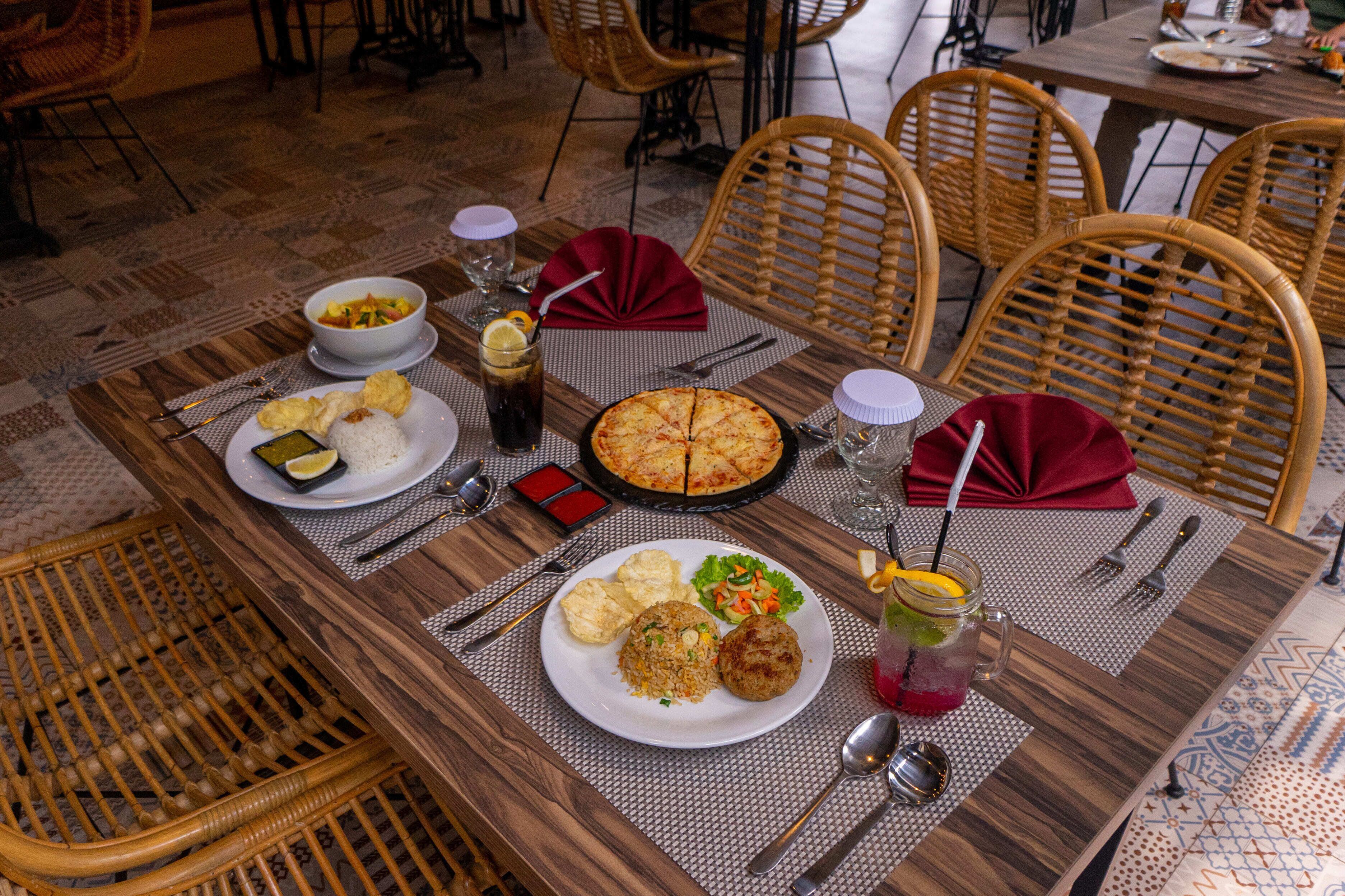 Una mesa de comedor dispuesta con platos de comida, incluyendo pastel, arroz y verduras, junto con bebidas y cubiertos.