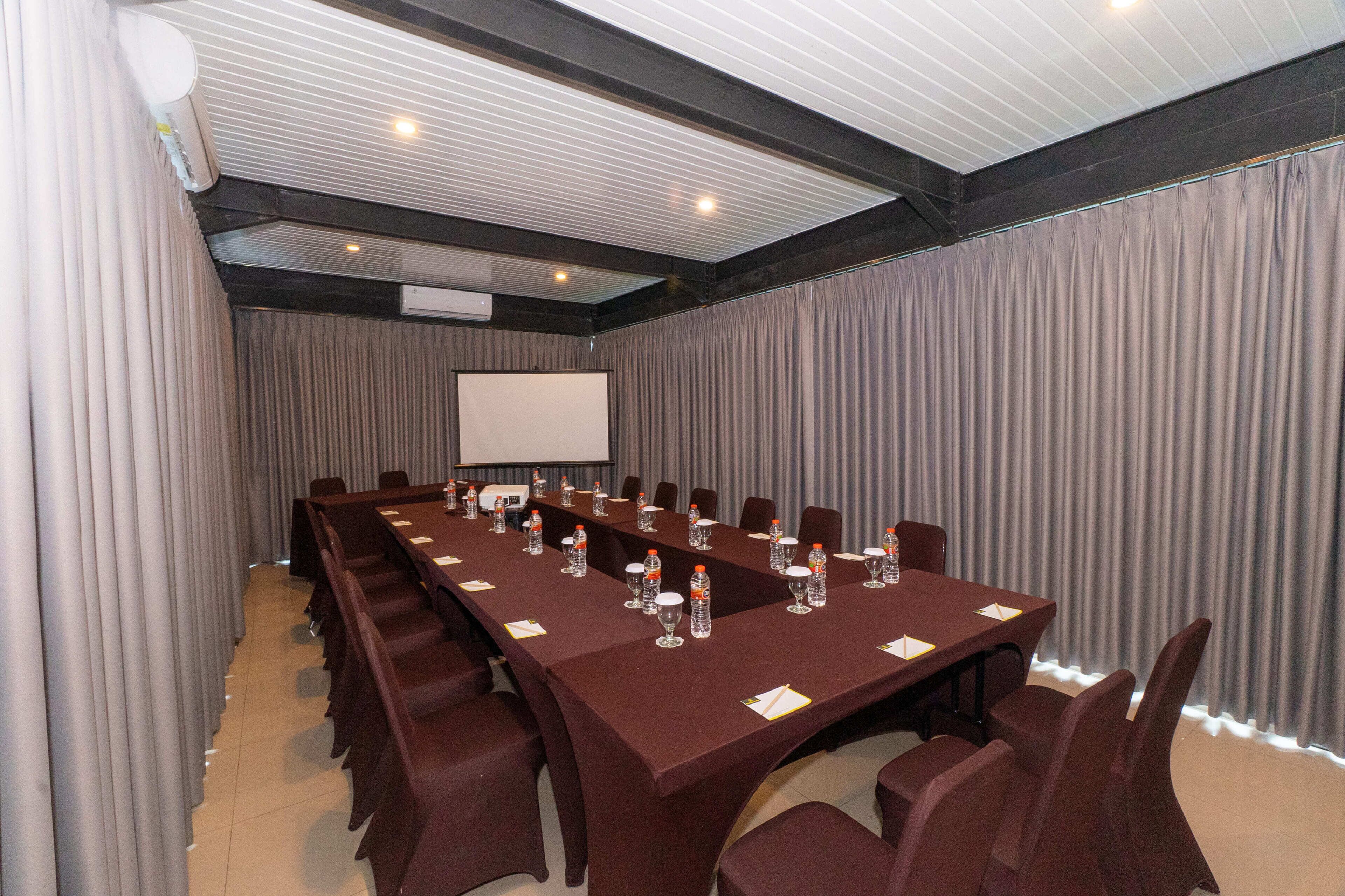 Una sala de conferències amb una taula llarga, cadires, ampolles d'aigua i una pantalla projectora.