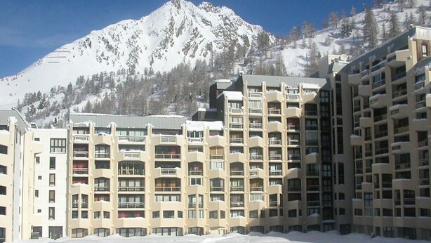 Ett hotell med flera våningar och balkonger, beläget med en snötäckt bergskedja som bakgrund.