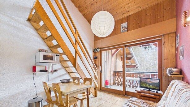 A cozy cabin interior with a dining area, a sofa, a TV, and a wooden staircase.