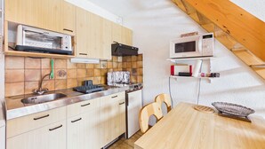 A compact kitchen with wooden cabinets, a built-in stove, a microwave, and a dining area with a wooden table and chairs.