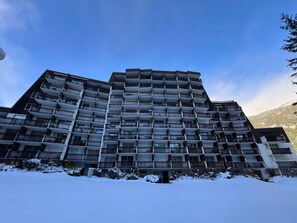 Hotel de vários andares com varandas, chão coberto de neve e céu limpo.