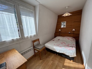 Um quarto com cabeceira de madeira, cama com roupa de cama floral, uma cadeira, uma escrivaninha e um radiador.