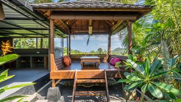 Relax in a serene outdoor seating area surrounded by lush tropical plants and a view of the surrounding hills.