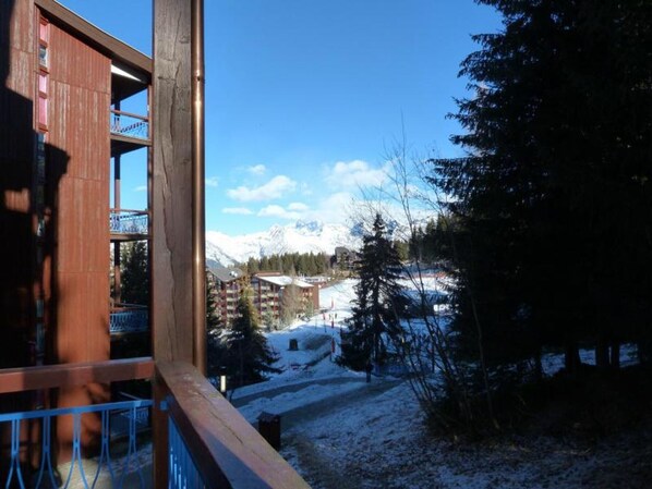 Une vue depuis une fenêtre donnant sur un paysage montagneux enneigé, avec des bâtiments en arrière-plan.