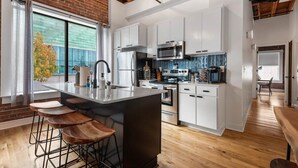 A modern kitchen with white cabinets, a large island with stools, and a view of the outdoors through a large window.