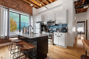 A modern kitchen with white cabinets, a large island with stools, and a view of the outdoors through a large window.