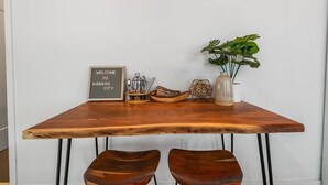 Une table en bois sur laquelle est posée une pancarte indiquant « BIENVENUE À KANSAS CITY », deux chaises en bois, une plante et un objet décoratif.
