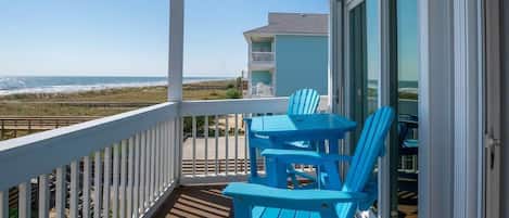 A balcony with a view of the beach, featuring a table and two chairs.