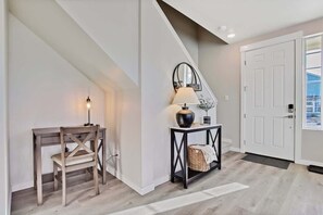 A hallway with a wooden bench, a table with a lamp, a mirror, and a door. - Stylish 2 bedroom townhome (Nampa)