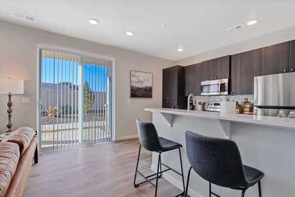 A modern kitchen with dark cabinets, a stainless steel refrigerator, and a bar area with two stools.