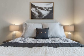 Ein Bett mit floralem Bettbezug, zwei Nachttischlampen und ein gerahmtes Bild von einer Berglandschaft.