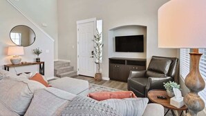 A spacious living room with a sofa, armchair, and a television mounted on the wall.
