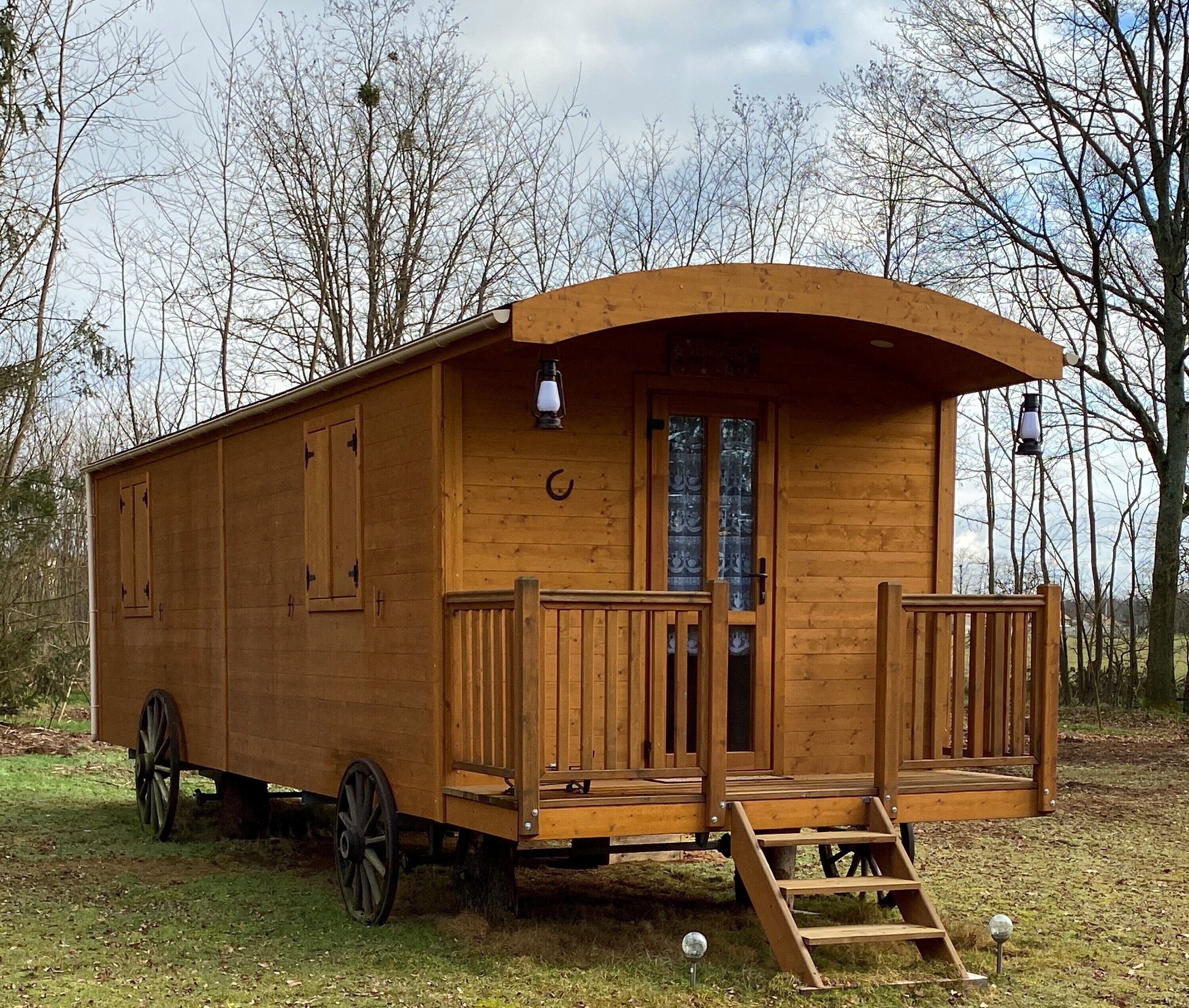 A wooden cabin with a curved roof, a front porch with steps, and a carriage wheel attached to the side.