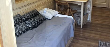 A cozy wooden cabin room with a bed, a desk, and a mirror on the wall.