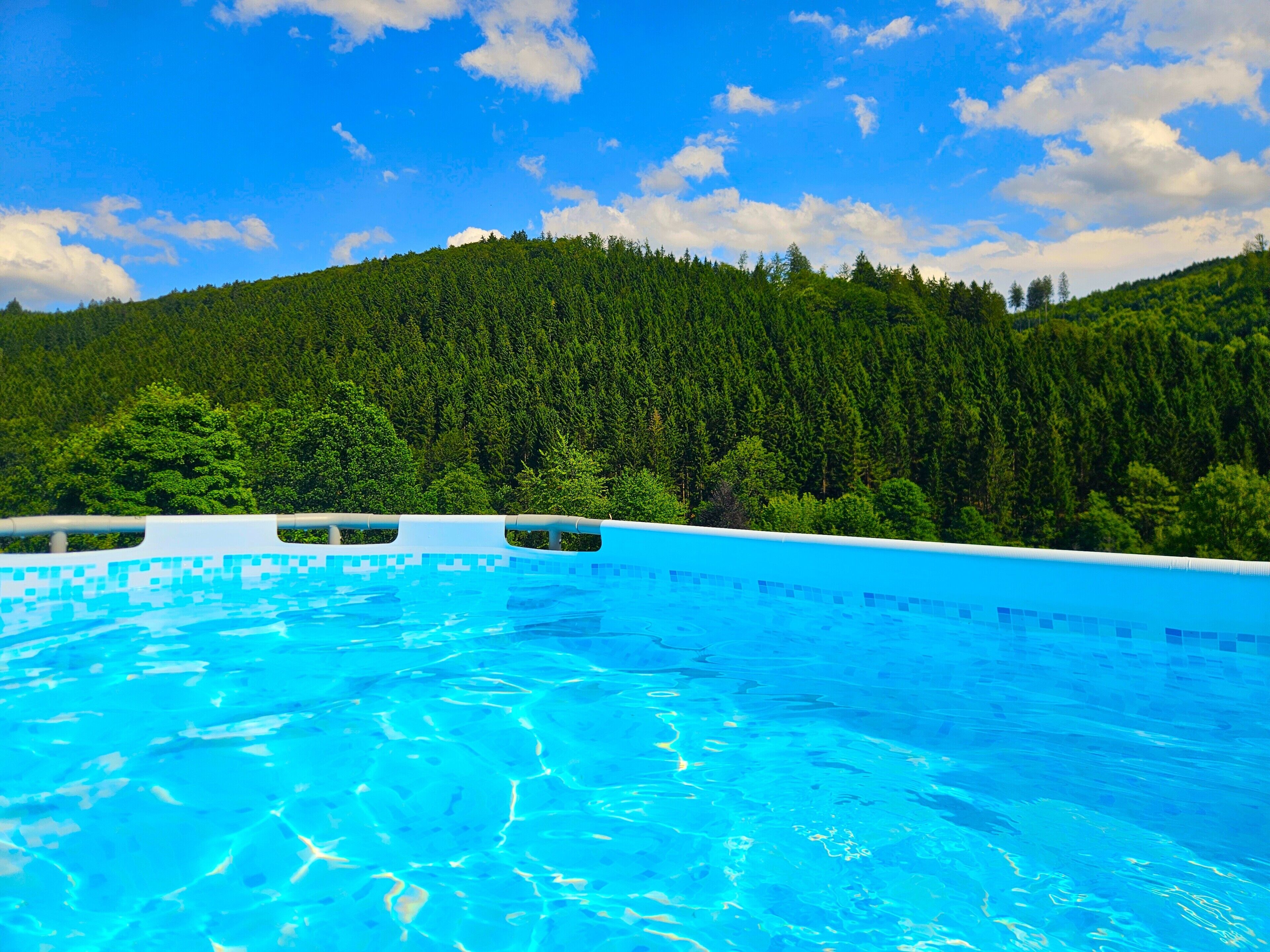 Ein Schwimmbecken mit klarem, blauem Wasser, umgeben von einem bewaldeten Hügelhang.