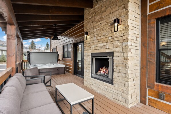 An outdoor patio with a stone fireplace, a sofa, and a table. - Rocky Mountain Gem!  Fireplace and Private Jacuzzi, Two Large patios, (Estes Park)