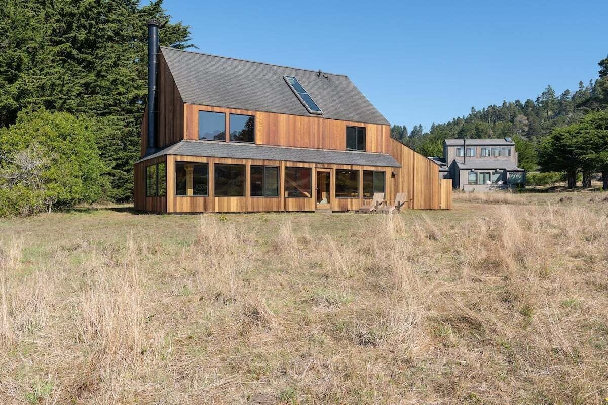 A modern wooden house with a sloped roof, large windows, and a chimney.