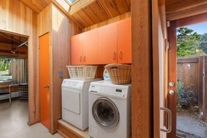 A laundry room with two washing machines, wooden cabinets, and a basket on top of one machine.