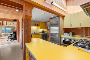 A modern kitchen with wooden beams, a yellow countertop, stainless steel appliances, and a view of the outdoors. - Binker Barn Reimagined | Sea Ranch Art (Sea Ranch)