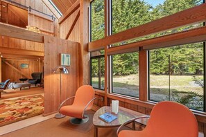 A wooden interior with a large window, orange chairs, and a small table. - Binker Barn Reimagined | Sea Ranch Art (Sea Ranch)
