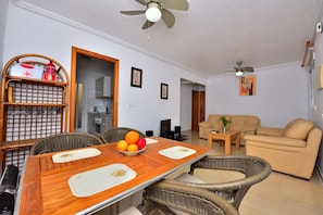 A dining area with a wooden table, wicker chairs, a bowl of fruit, and a ceiling fan. - Holiday Home "Casa Butcher" with Mountain View, Terraces & Wi-Fi (Mazarrón)