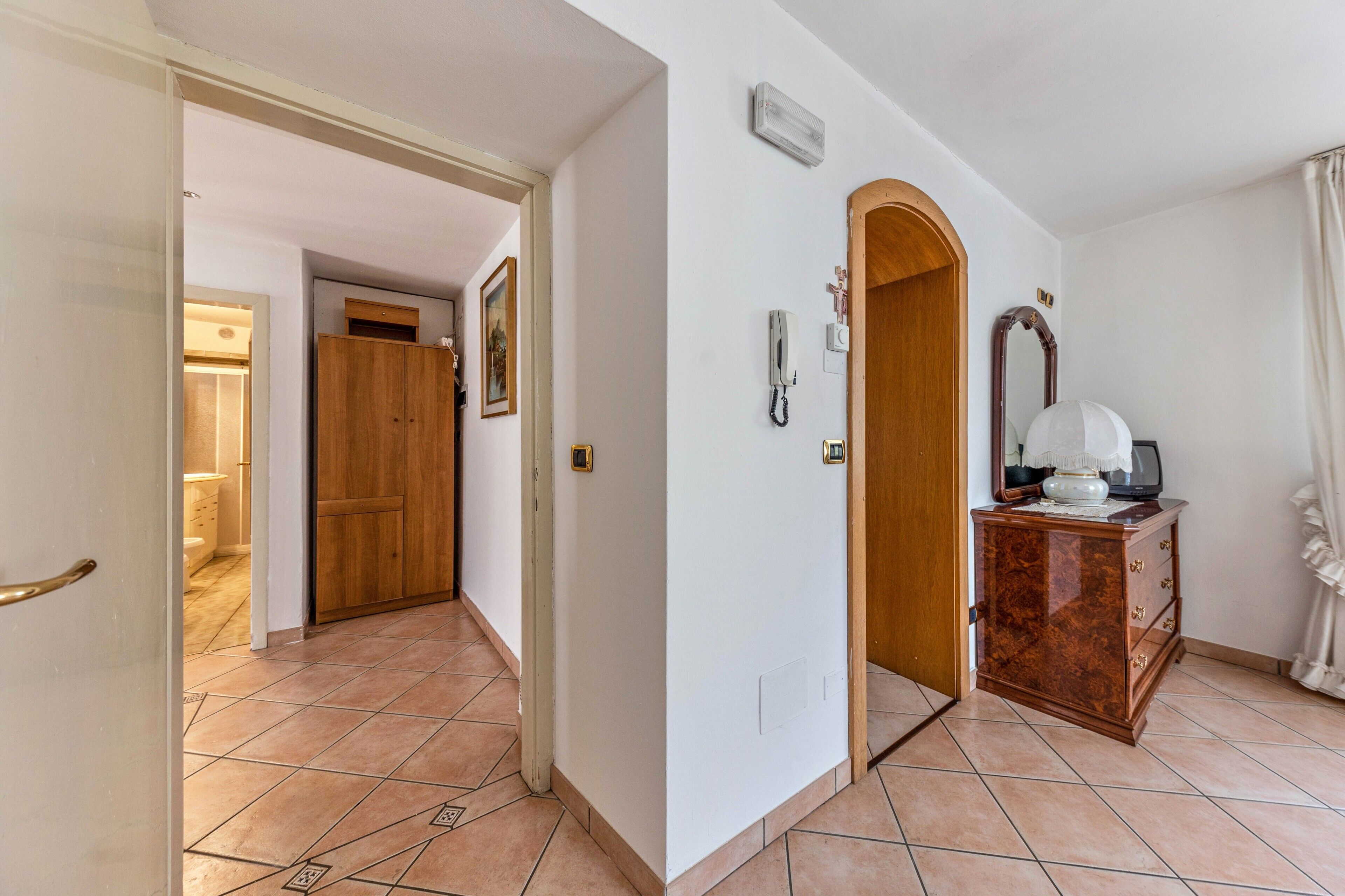 Um corredor com porta de madeira, espelho, telefone e um pequeno armário.